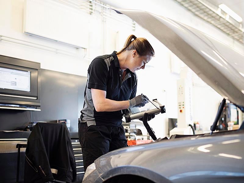 Un técnico de servicio está inspeccionando el compartimento del motor y tomando notas.